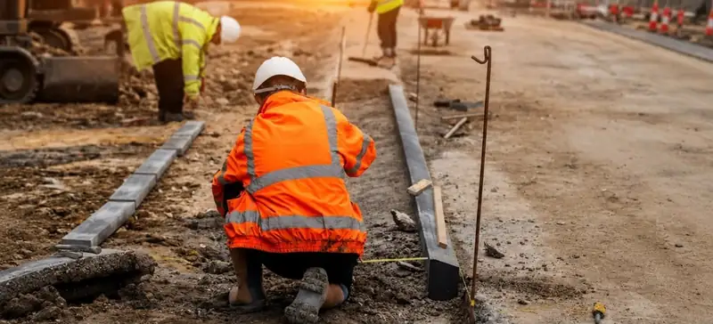A groundworker in orange hi-vis laying kerbs on a new road